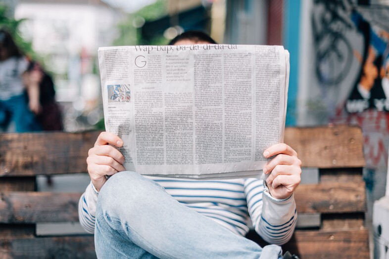 Man reads newspaper on a bench.