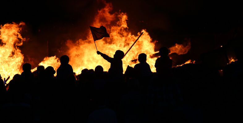 A photo of rioters standing in front of a fire