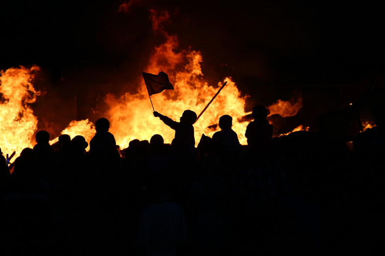 A photo of rioters standing in front of a fire