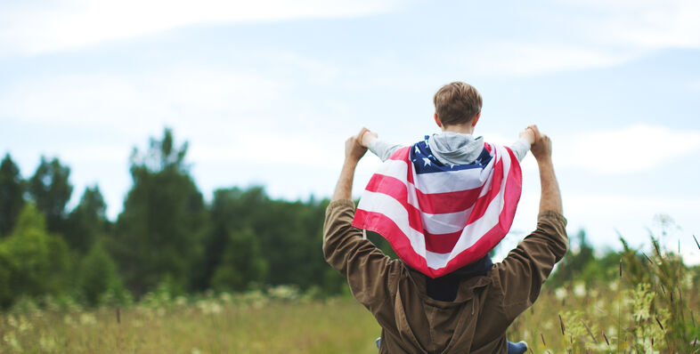 A child with an American flag cape on his father's back