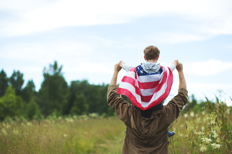 A child with an American flag cape on his father's back